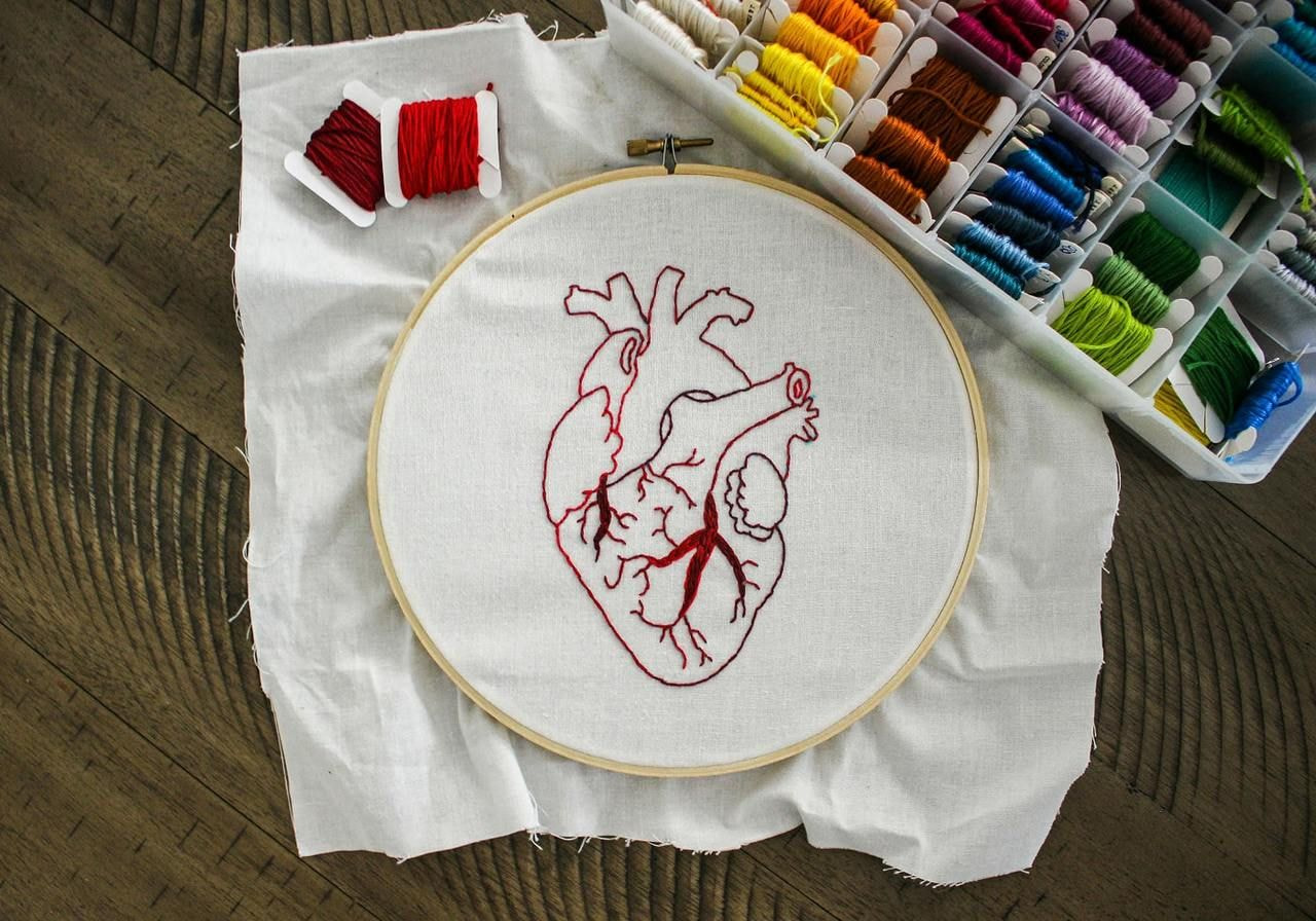 Heart-shaped embroidery displayed on a rustic wooden table, showcasing intricate stitching and vibrant thread colors.